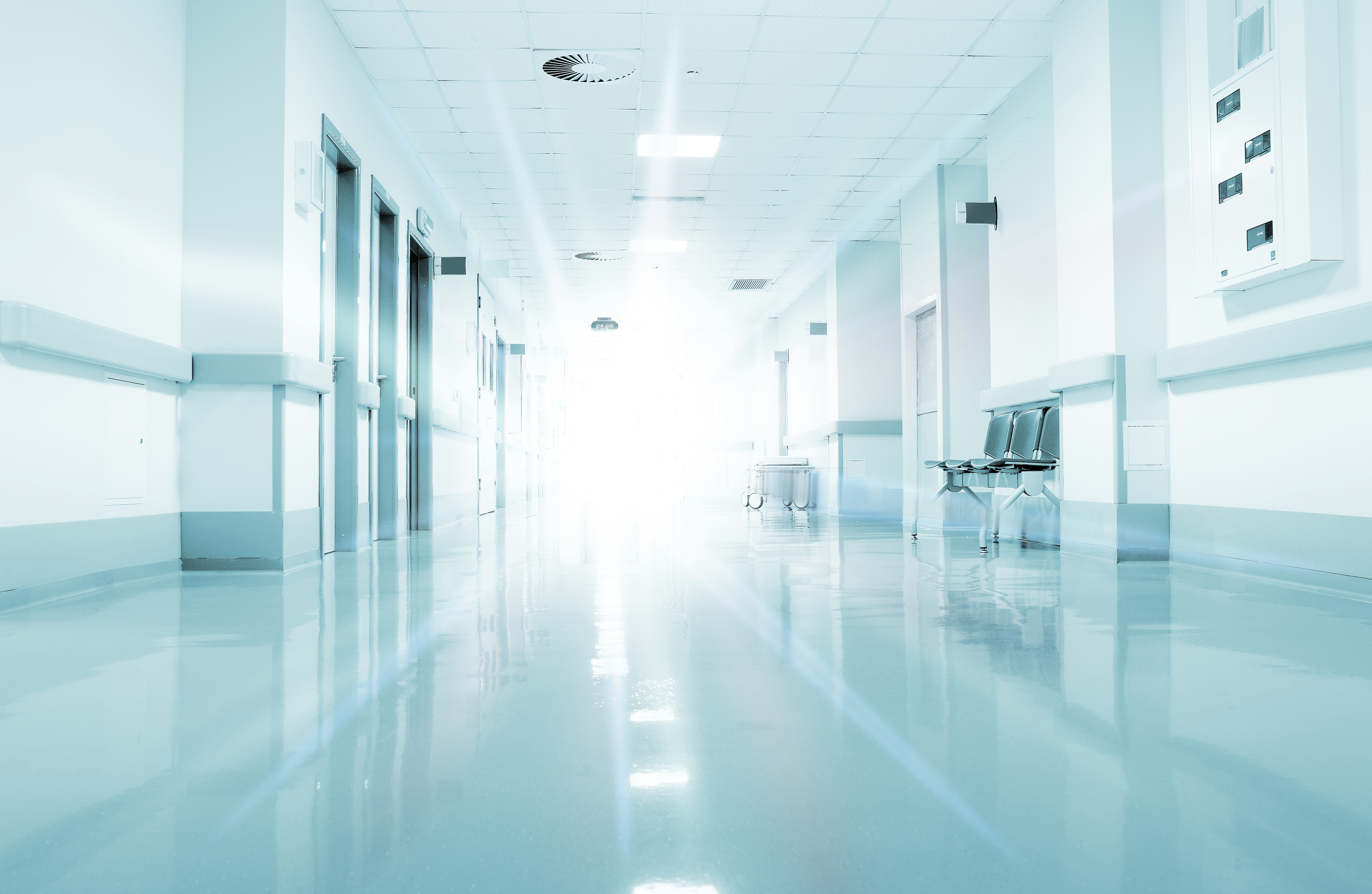 Bright, empty hospital hallway with reflective floors and doors lining both sides.