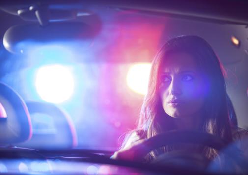 A driver inside a car with police lights flashing behind the vehicle.