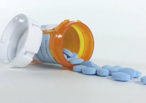 Orange prescription bottle tipped over with blue oval pills spilling onto a white surface.