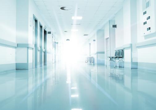 Bright, empty hospital hallway with reflective floors and doors lining both sides.