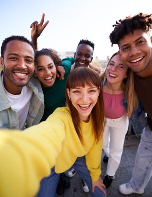 Un groupe de jeunes divers prenant un selfie à l'extérieur, s'amusant par une journée ensoleillée.