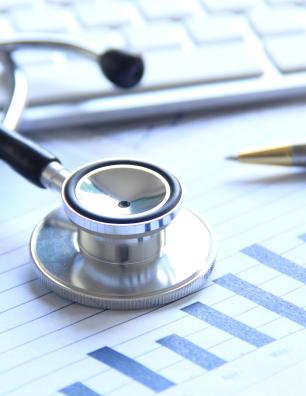 Stéthoscope et stylo posés sur des dossiers médicaux, à côté du clavier d’un ordinateur. 