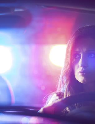 Conductrice assise dans une voiture avec des gyrophares de police illuminant le véhicule.