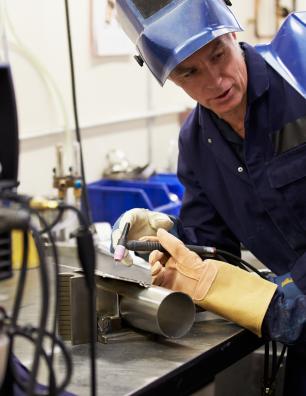 Two workers in protective gear welding a metal pipe in an industrial workshop setting.