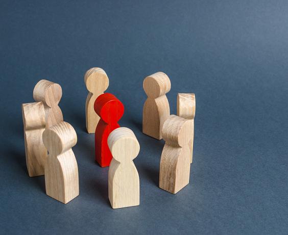 Figurines en bois disposées en cercle entourant une seule figurine rouge.
