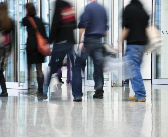 Personnes floues qui marchent dans le hall d’entrée moderne en verre d’un immeuble urbain achalandé.